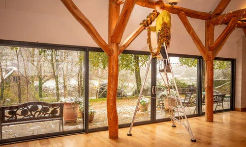 Person hanging tinsel from beams while on a ladder