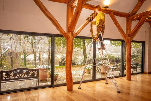 Person hanging tinsel from beams while on a ladder