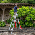 A person using a garden platform to trim a shrub