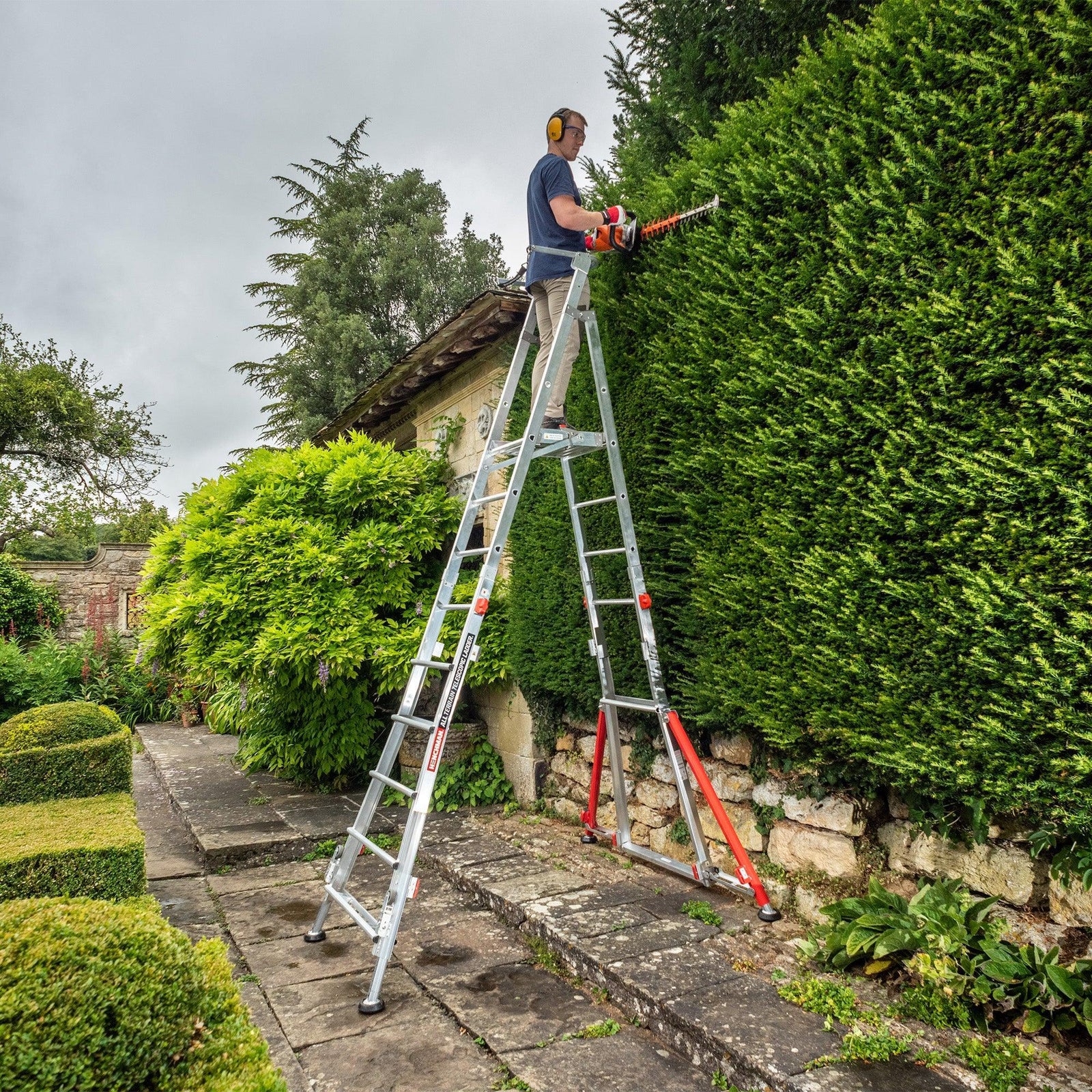 A person standing on a fully extended All Terrain Platform to trim a hedge