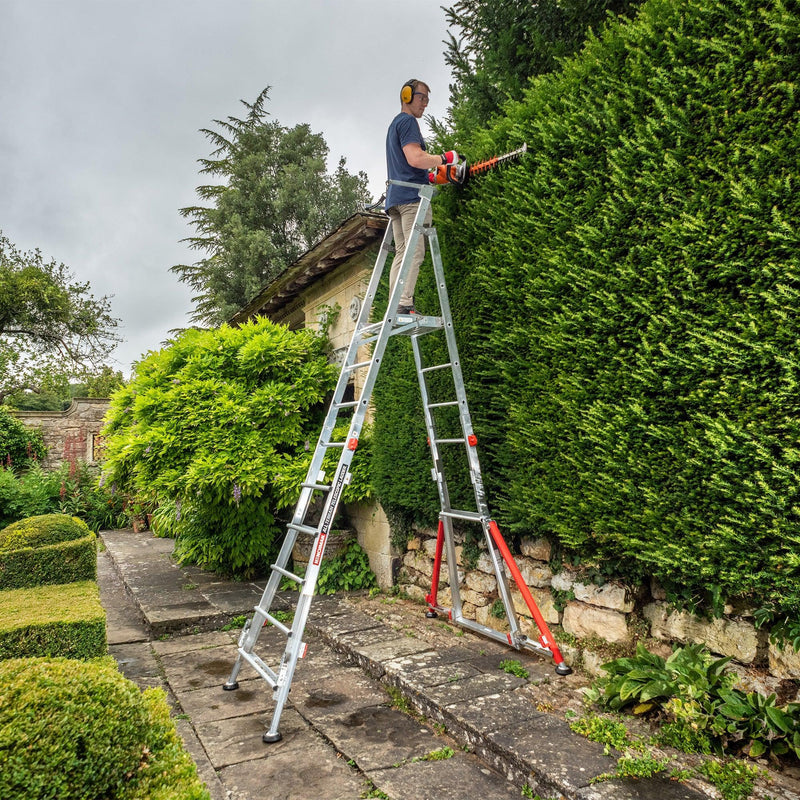 A person standing on a fully extended All Terrain Platform to trim a hedge