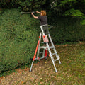 A person standing on a work platform to trim a hedge