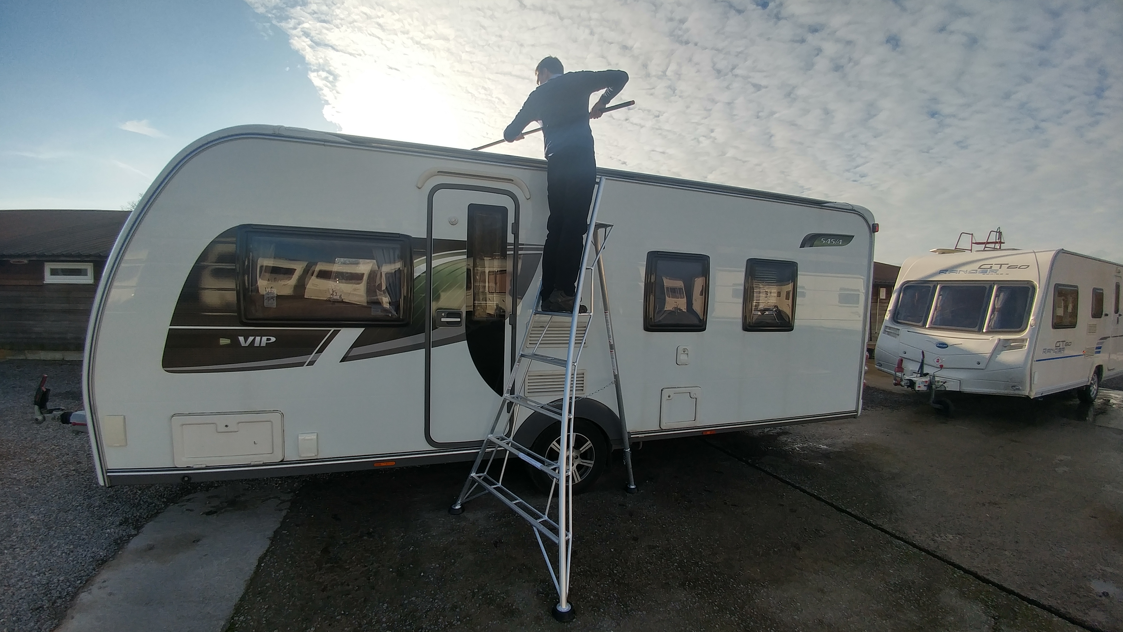 Man cleaning caravan roof with tripod ladder